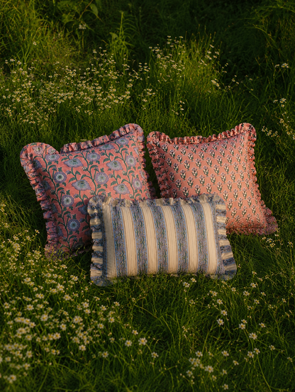 Three ruffled floral and striped cushions from the Razia, Yavi and Taj collection sit in tall grass with white wildflowers at golden hour.