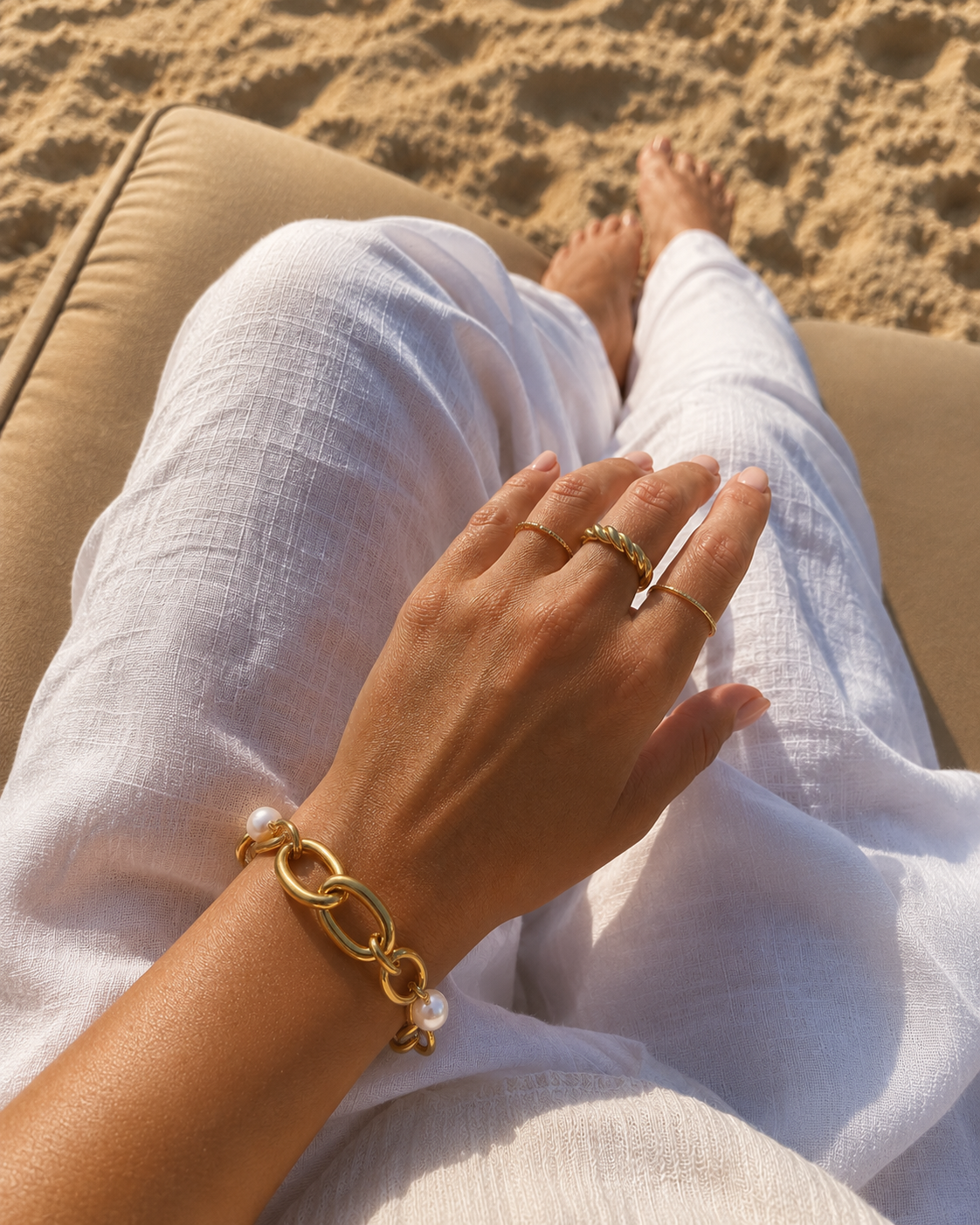 Reckless BRACELET worn on the wrist with its chunky gold links and pearls, model relaxing on a lounger at the beach.