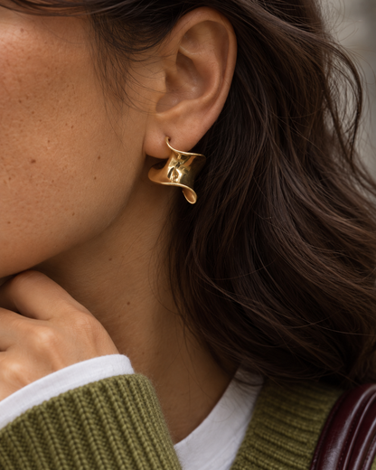 Close-up of a gold Ribbon EARRING, a twisted ribbon-shaped stud, on a woman in an olive knit — Folie à Trois