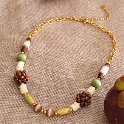 The Rio NECKLACE laid on woven fabric beside a carved wooden figure, its jade and wood cluster beads shown in close detail.