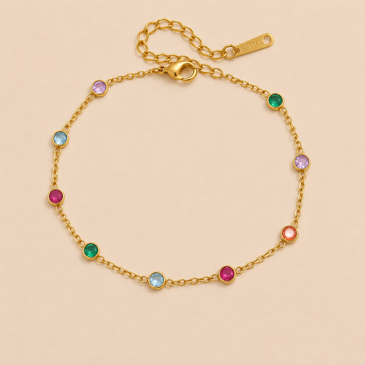 Riva BRACELET in gold with round multicolored gemstones evenly spaced along a fine chain, shown flat on a beige background.