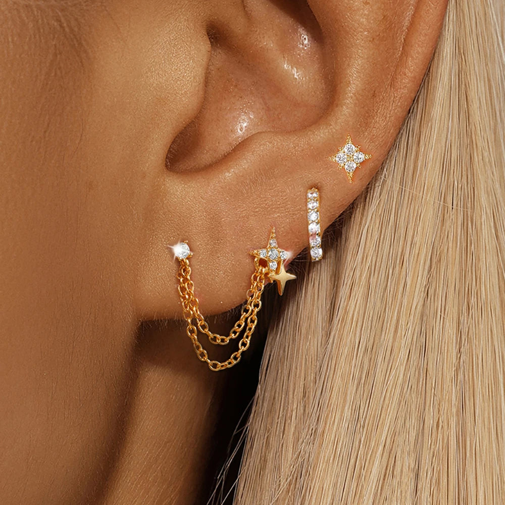 Close-up of an ear wearing the gold Romy SET: a chain-linked double star stud, a pavé huggie hoop and a four-point star stud.