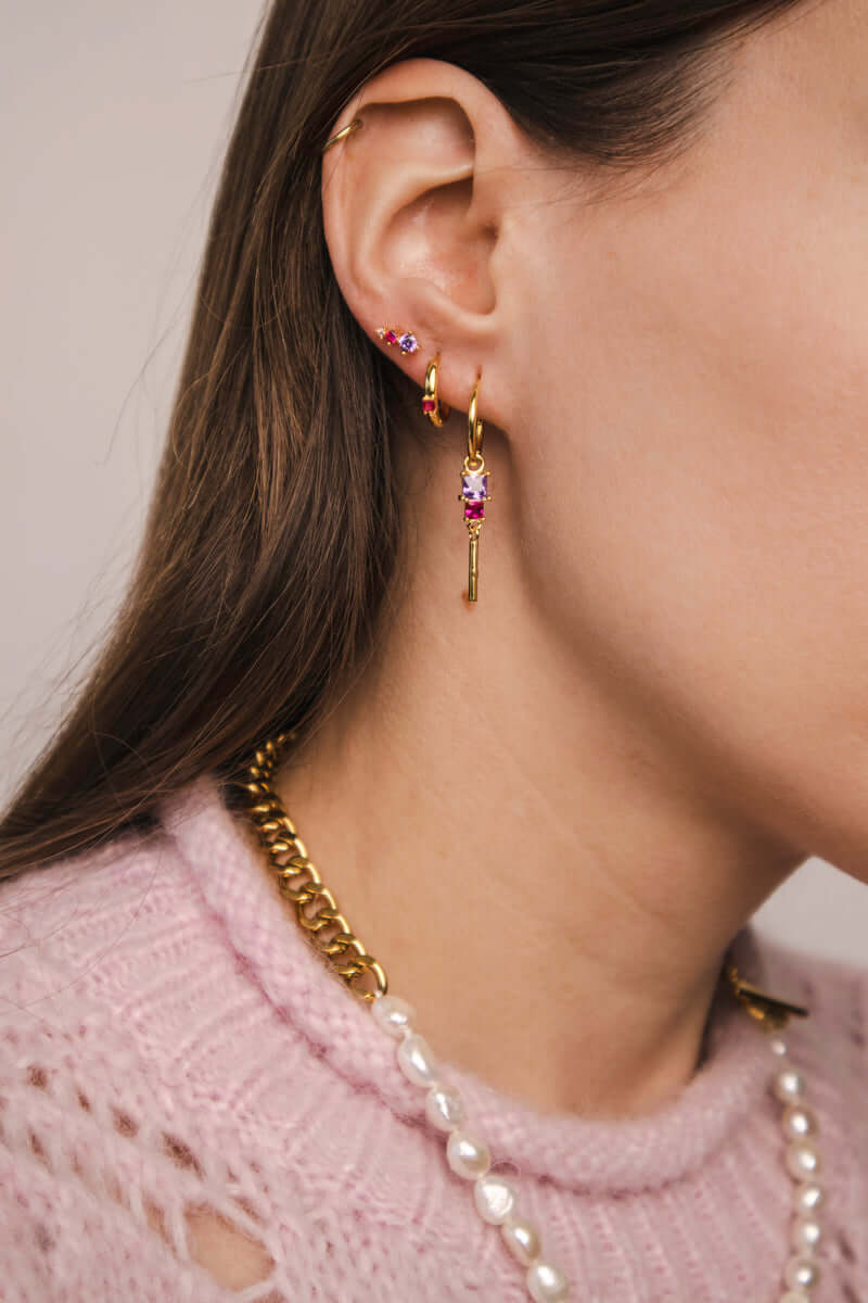 A model wears the Rosa SET in gold with lilac and pink stones, layering the bar-dangle hoop earring among other ear piercings.