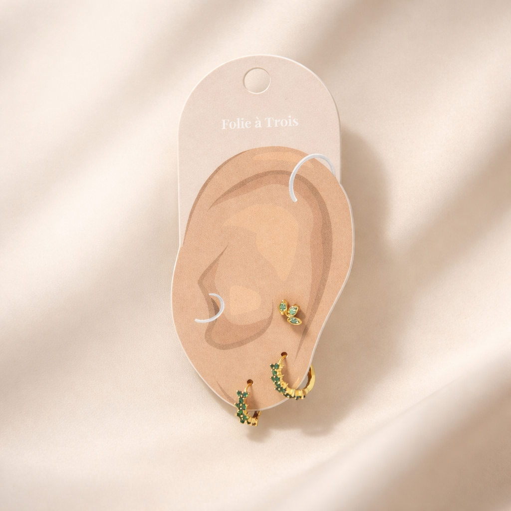 Rosalia Set displayed on a Folie a Trois ear-shaped card in gold, arranging the flower stud and two green pave hoops.