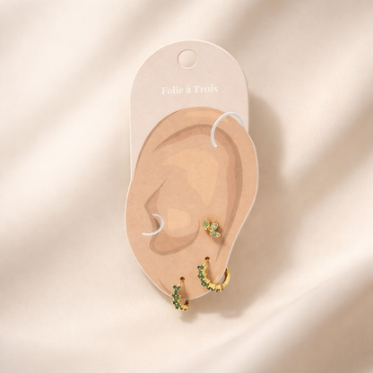 Rosalia Set displayed on a Folie a Trois ear-shaped card in gold, arranging the flower stud and two green pave hoops.