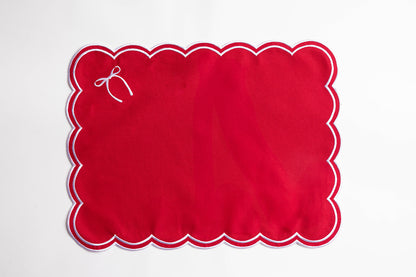 Flat lay of a red rectangular placemat with white scalloped trim and a small embroidered white bow, the Rosie Scallop placemat with bow.