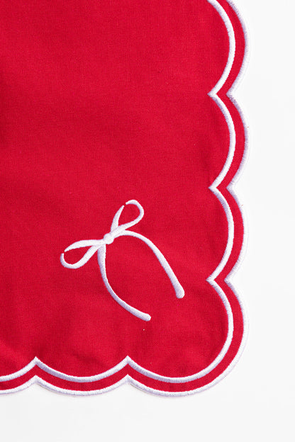 Close-up of a red napkin corner with white scalloped trim and a delicate embroidered bow, from the Rosie Scallop napkins with bow.