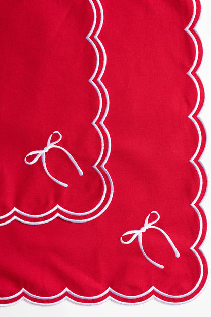 Close-up of overlapping red napkin corners with white scalloped trim and an embroidered bow, from the Rosie Scallop napkins with bow.