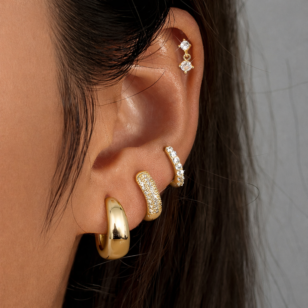 Roxy Set in gold worn on the ear, a cartilage drop stud above a stack of pave and chunky teardrop hoops.