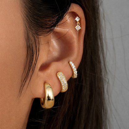 Roxy Set in gold worn on the ear, a cartilage drop stud above a stack of pave and chunky teardrop hoops.
