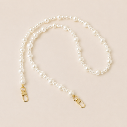 Folie à Trois Sabine Pearl long wholesale phone chain in graduated white pearls with gold clasps, coiled on a cream background.