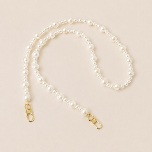 Folie à Trois Sabine Pearl long wholesale phone chain in graduated white pearls with gold clasps, coiled on a cream background.