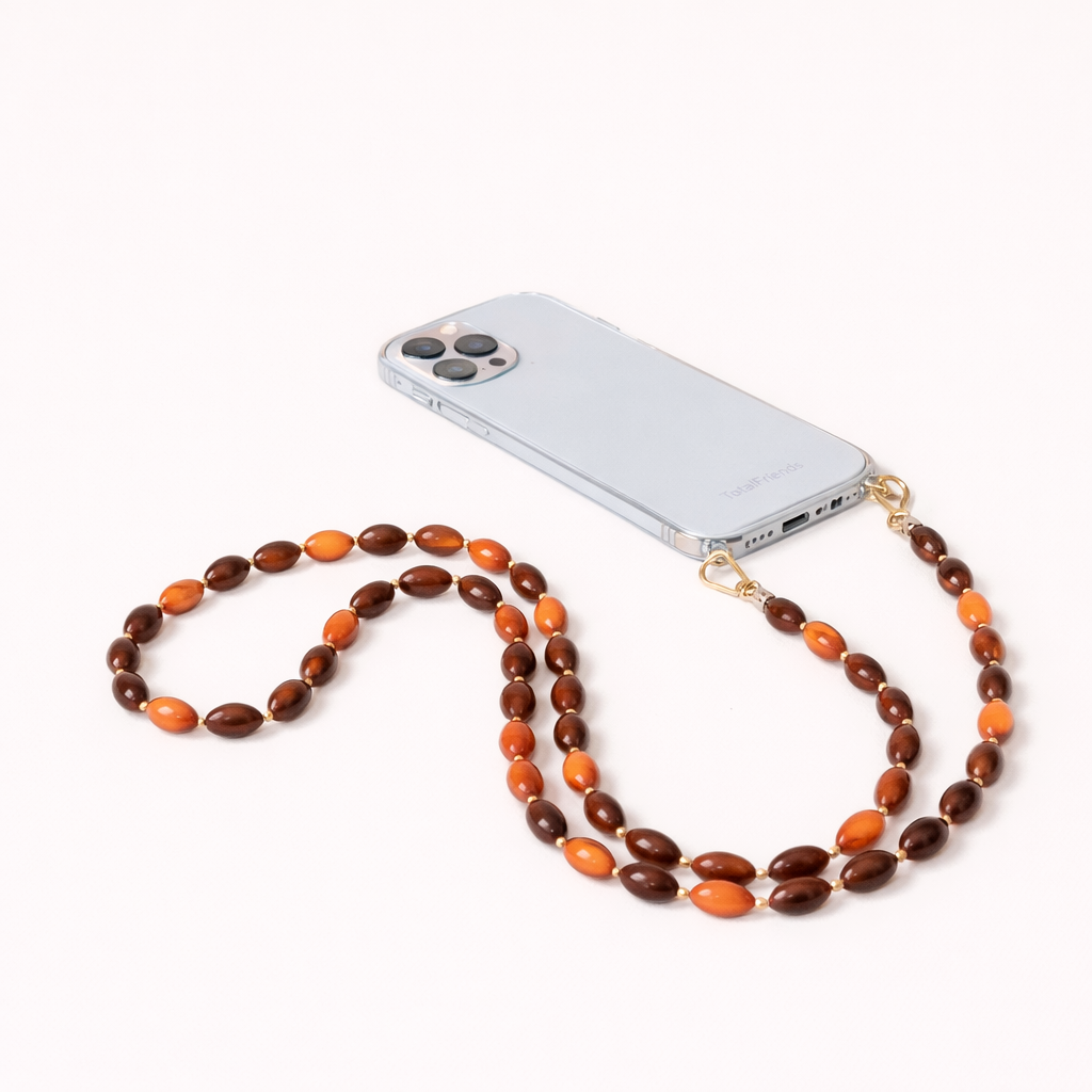 Saffron Long Phone Strap in amber and brown oval beads, clipped to a clear phone case with gold hardware.