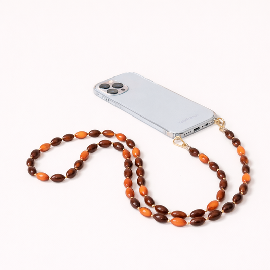 Saffron Long Phone Strap in amber and brown oval beads, clipped to a clear phone case with gold hardware.