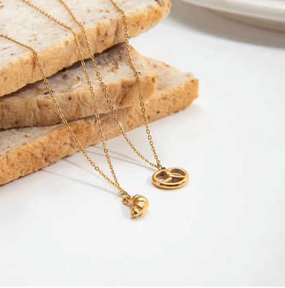 The Salty Sweet NECKLACE and its matching croissant charm necklace draped over slices of bread on a white surface.