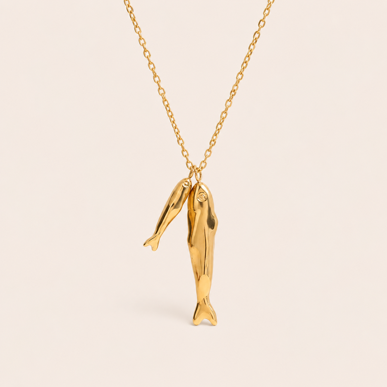 Gold chain necklace with two textured sardine fish charms from the Sardina NECKLACE design, laid flat on beige.