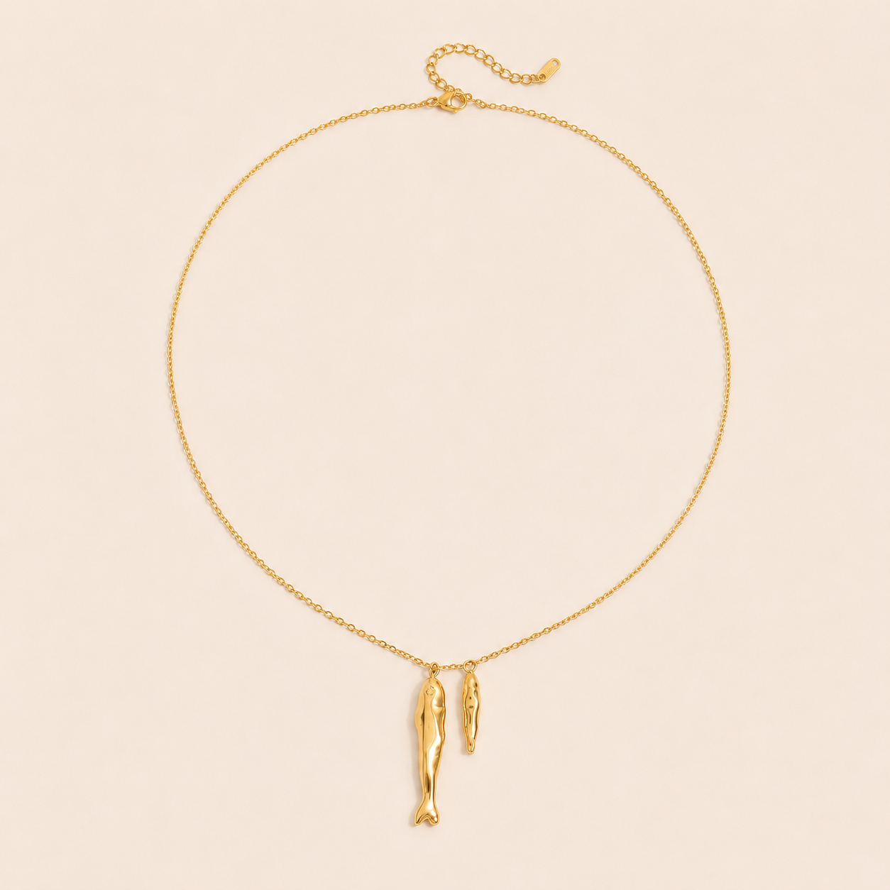 Gold Sardina NECKLACE with two fish charms and an adjustable clasp, shown fastened in a circle on a beige background.