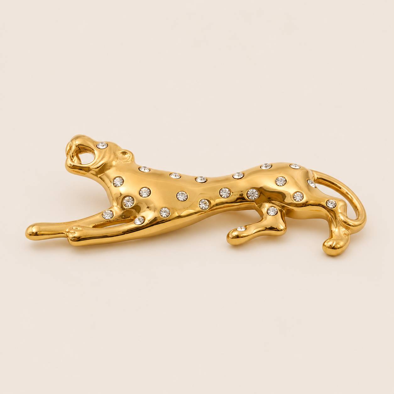 Gold leopard-shaped brooch with crystal spots in a leaping pose on a cream backdrop — Folie à Trois Savana BROOCH