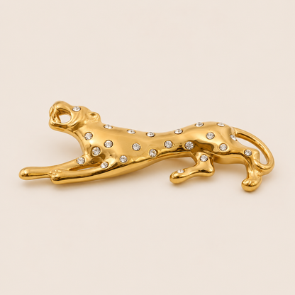 Gold leopard-shaped brooch with crystal spots in a leaping pose on a cream backdrop — Folie à Trois Savana BROOCH