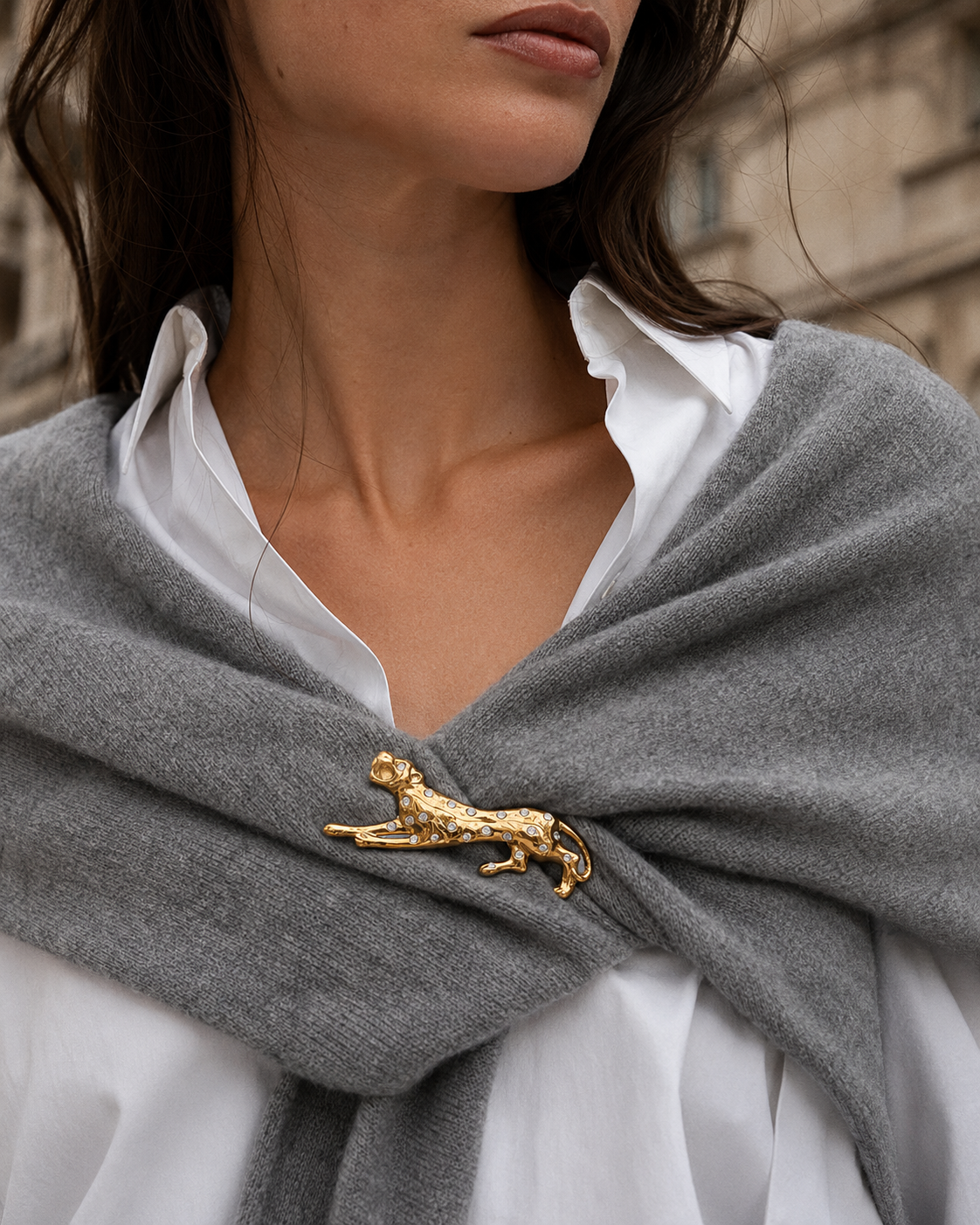 Close-up of a model pinning a gold leopard Savana BROOCH to a grey wrap over a white shirt outdoors — Folie à Trois