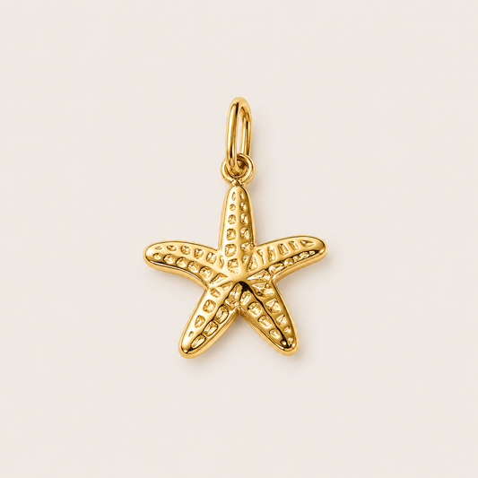 The Seastar CHARM in gold, a textured starfish pendant with a beaded surface, shown in close-up studio photography on cream.