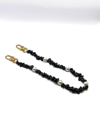 Black beaded Shell Whisper SHORT PHONE STRAP laid flat with gold-tone clasps on a white background.