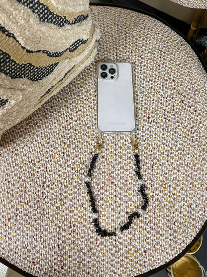 Black beaded Shell Whisper SHORT PHONE STRAP attached to a phone, resting on a tweed ottoman.
