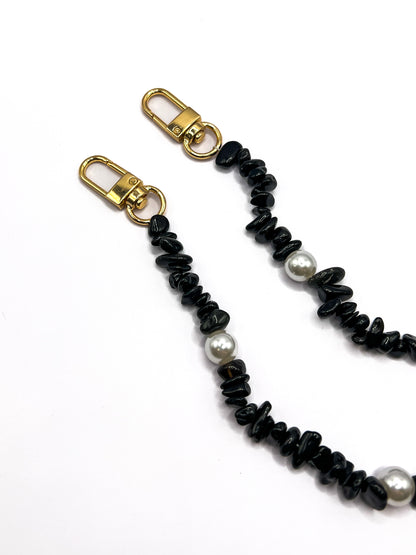 Close-up of a black beaded Shell Whisper SHORT PHONE STRAP with gold-tone clasps, laid flat on a white background.
