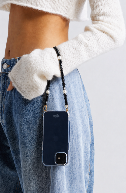 Black beaded Shell Whisper SHORT PHONE STRAP on a phone in a clear case, worn at the hip by a model in a cream sweater and jeans.