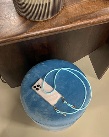 Clear phone case with a blue Shimmery PHONE CORD resting on a blue velvet ottoman.