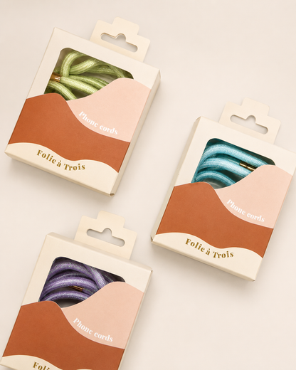 Three Shimmery PHONE CORD packaging boxes in green, blue, and purple, labeled Folie à Trois.
