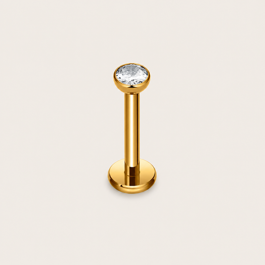 The Shine Bright PIERCING in gold, a labret-style stud set with a round clear gem, shown upright on a cream background.