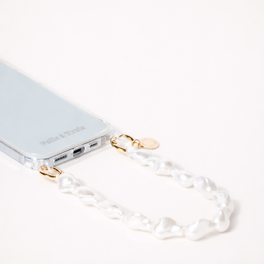 Clear phone case attached to a chunky baroque pearl Short Pearl PHONE STRAP with gold-tone clasps on a cream background.