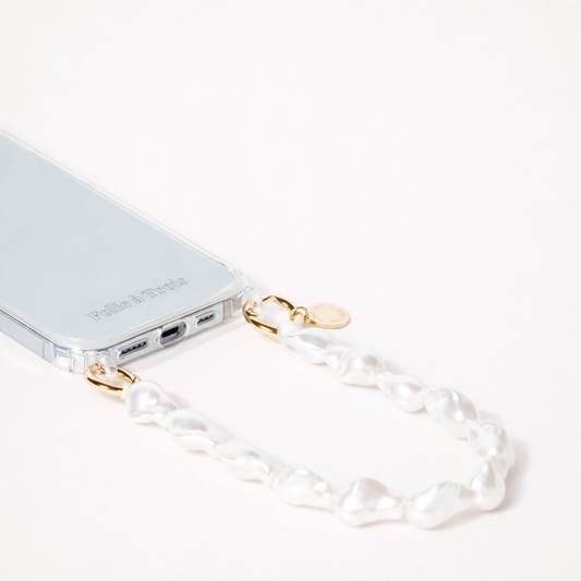 Clear phone case attached to a chunky baroque pearl Short Pearl PHONE STRAP with gold-tone clasps on a cream background.