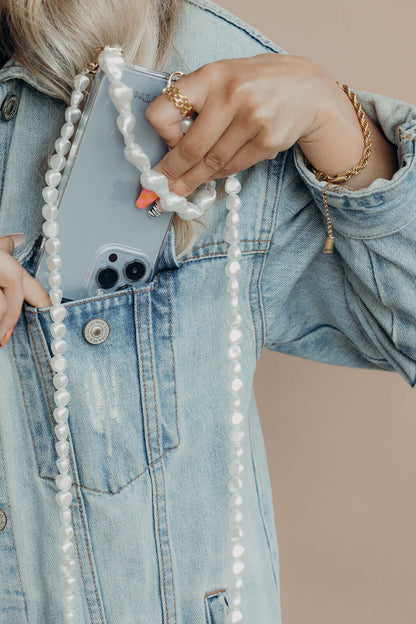Baroque pearl Short Pearl PHONE STRAP with the phone tucked into a denim jacket pocket, hand pulling it out, gold jewelry visible.
