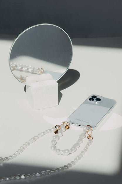 Baroque pearl Short Pearl PHONE STRAP and phone styled in sharp focus beside a round mirror on a marble stand.