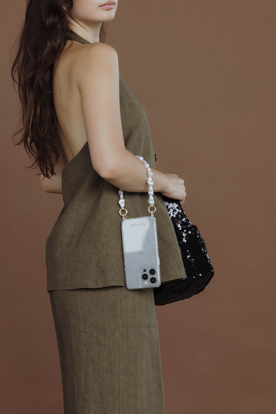 Woman seen from the side holding a black sequin bag with a phone case on a baroque pearl Short Pearl PHONE STRAP, khaki outfit.