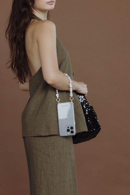 Woman seen from the side holding a black sequin bag with a phone case on a baroque pearl Short Pearl PHONE STRAP, khaki outfit.