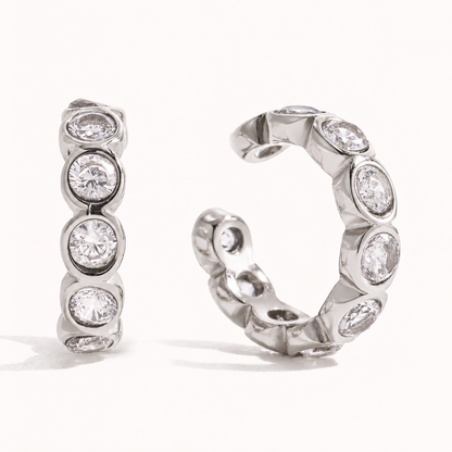 Pair of silver-tone ear cuffs lined with round bezel-set zirconia stones on a white background — Folie à Trois