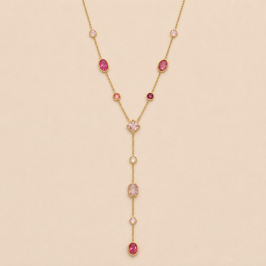 Gold Sirena Y NECKLACE with pink and red gemstone stations of mixed cuts, drawn into a long lariat drop, laid on a beige background.