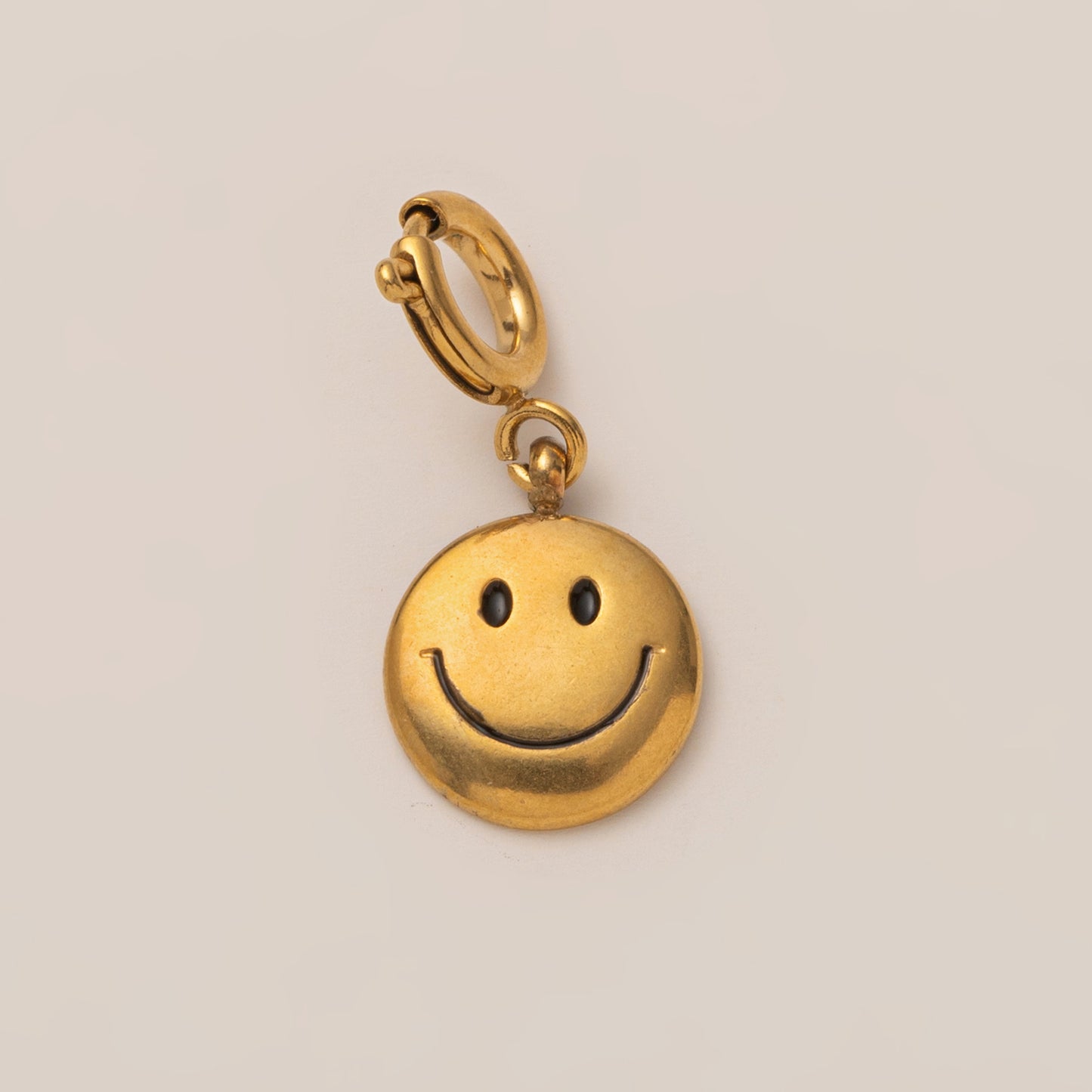 The Smiley Face CHARM in gold, a round pendant with black enamel eyes and smile, shown attached to a small hoop in close-up.