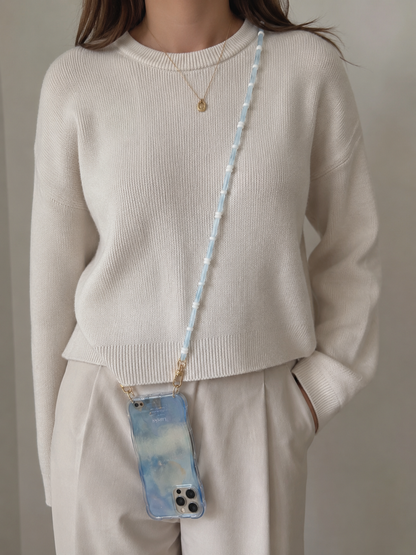 Woman wearing a light blue Smooth Moves PHONE CHAIN with a blue tie-dye phone case over a cream sweater.