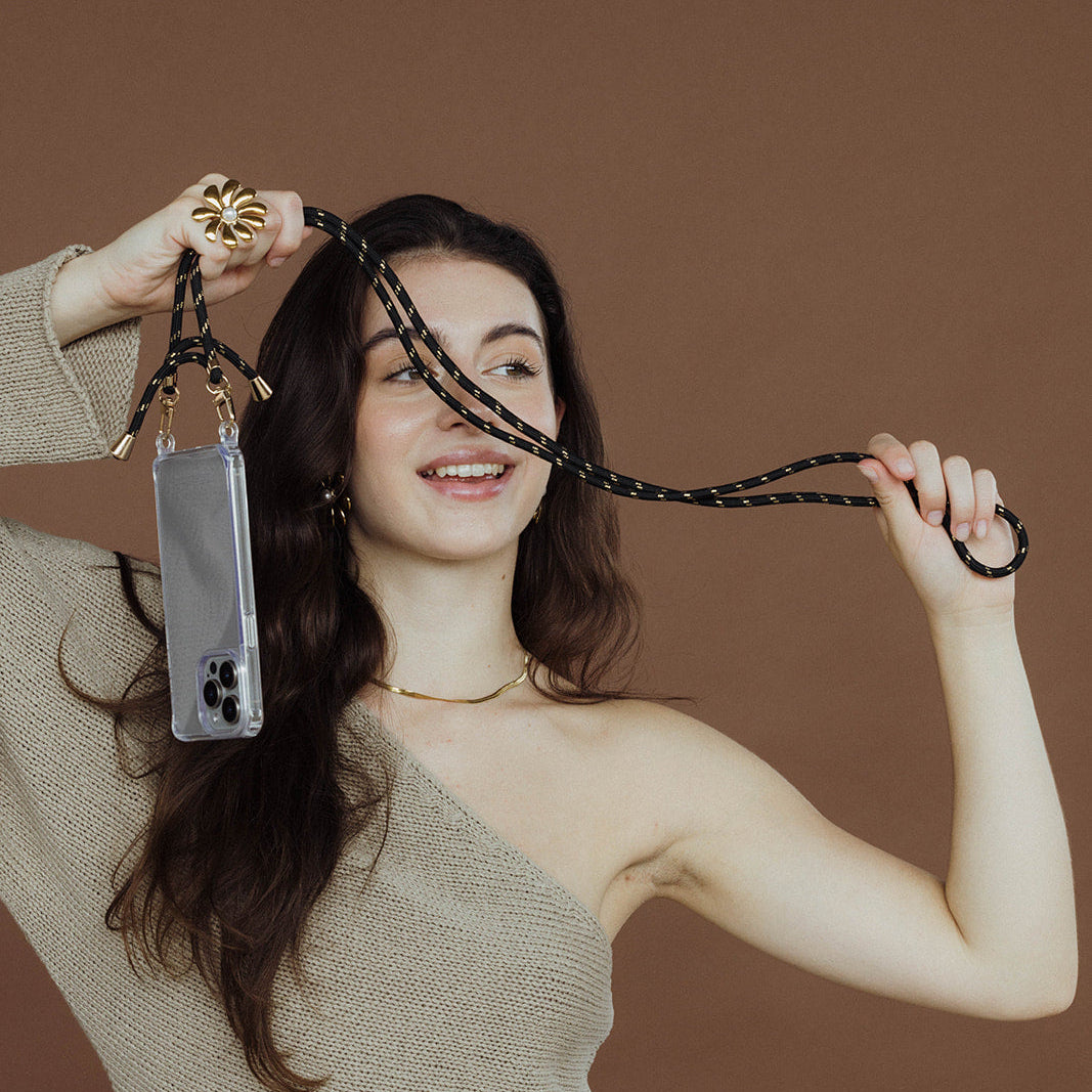The Snake Skin NECKLACE in gold worn faintly at the neckline while the model holds up a beaded phone strap and case.