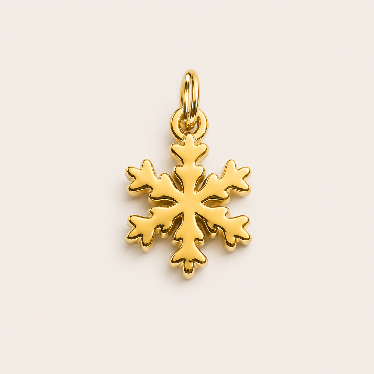 The Snowflake CHARM in gold, a detailed snowflake pendant with a jump ring, shown in close-up studio photography on cream.