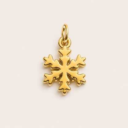 The Snowflake CHARM in gold, a detailed snowflake pendant with a jump ring, shown in close-up studio photography on cream.