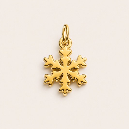 The Snowflake CHARM in gold, a detailed snowflake pendant with a jump ring, shown in close-up studio photography on cream.