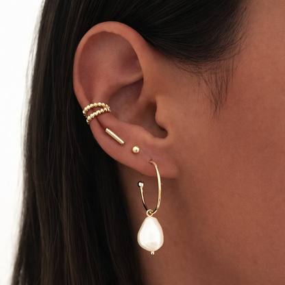 The Solara EARCUFF worn on the ear cartilage, a beaded gold cuff layered above a pearl drop hoop earring stack.