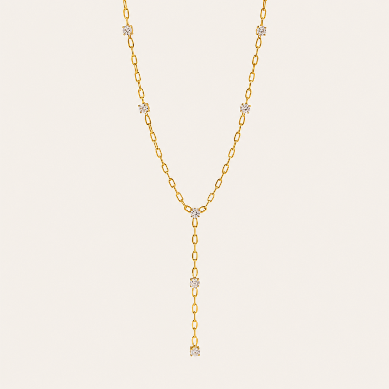 Gold paperclip-link Soleil Y NECKLACE with crystal stations drawn into a long lariat drop, laid flat on beige.