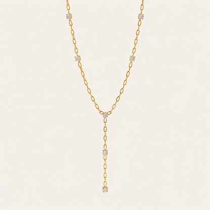 Gold paperclip-link Soleil Y NECKLACE with crystal stations drawn into a long lariat drop, laid flat on beige.