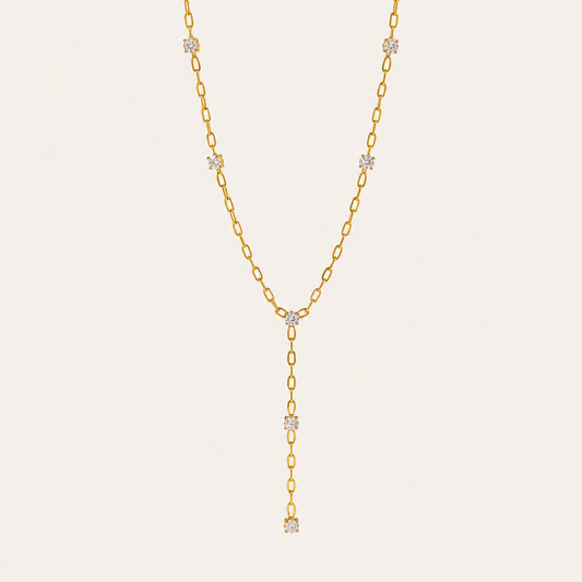 Gold paperclip-link Soleil Y NECKLACE with crystal stations drawn into a long lariat drop, laid flat on beige.